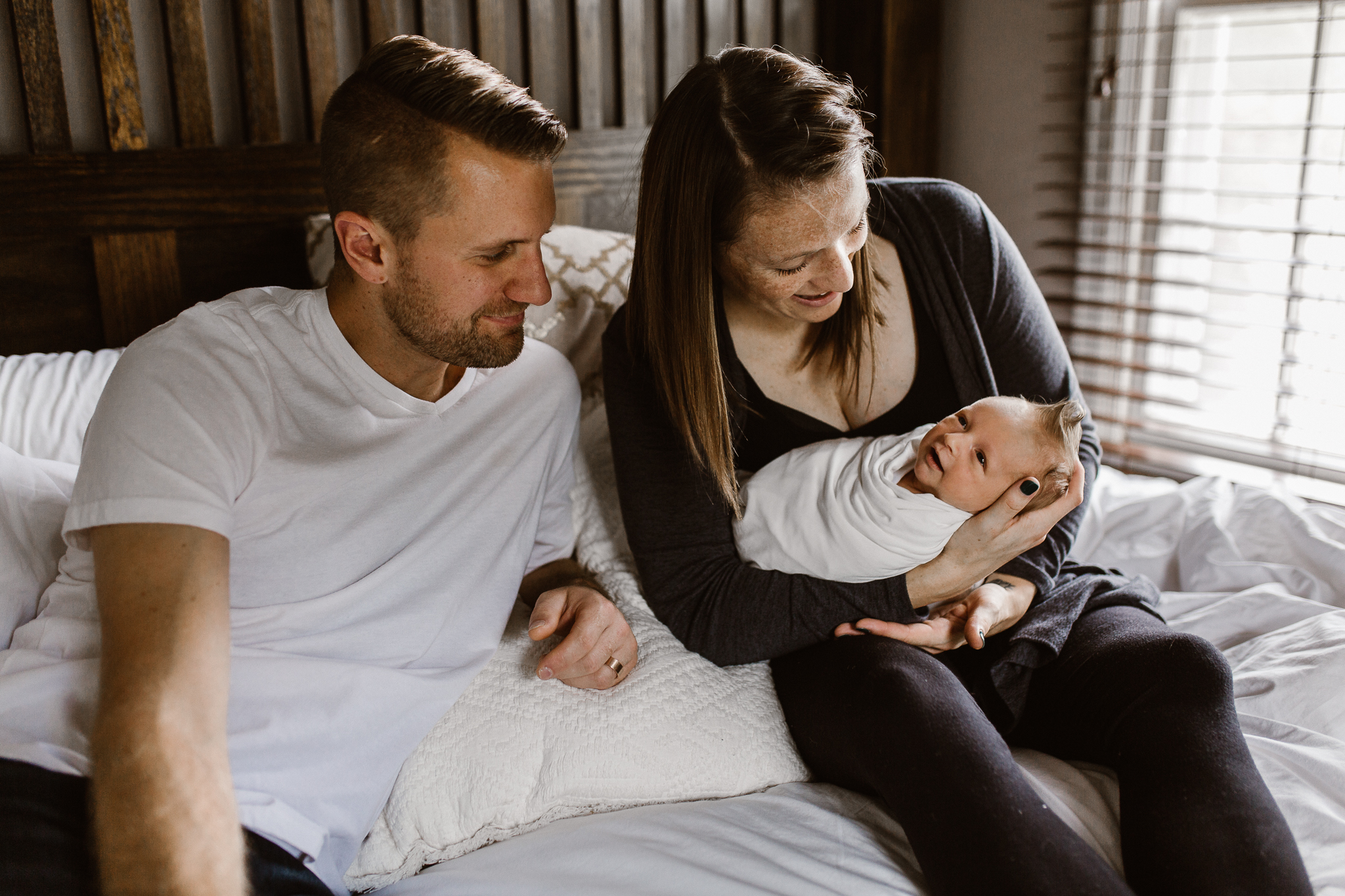 Newborn baby's parents admiring their son's facial expressions on their bed.